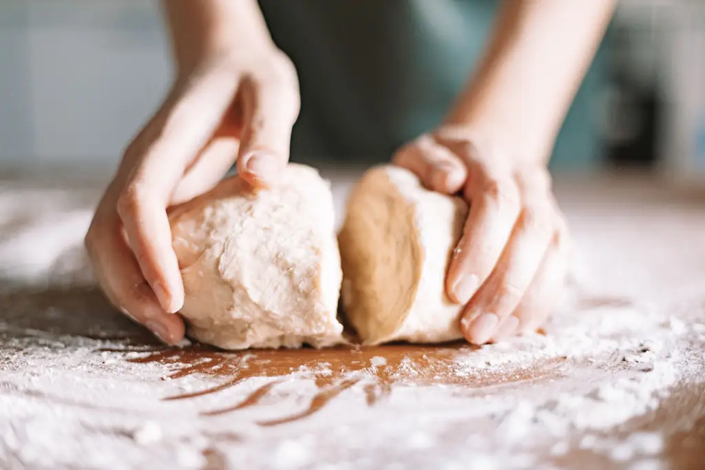 Hands kneading soft dough on a floured wooden bench